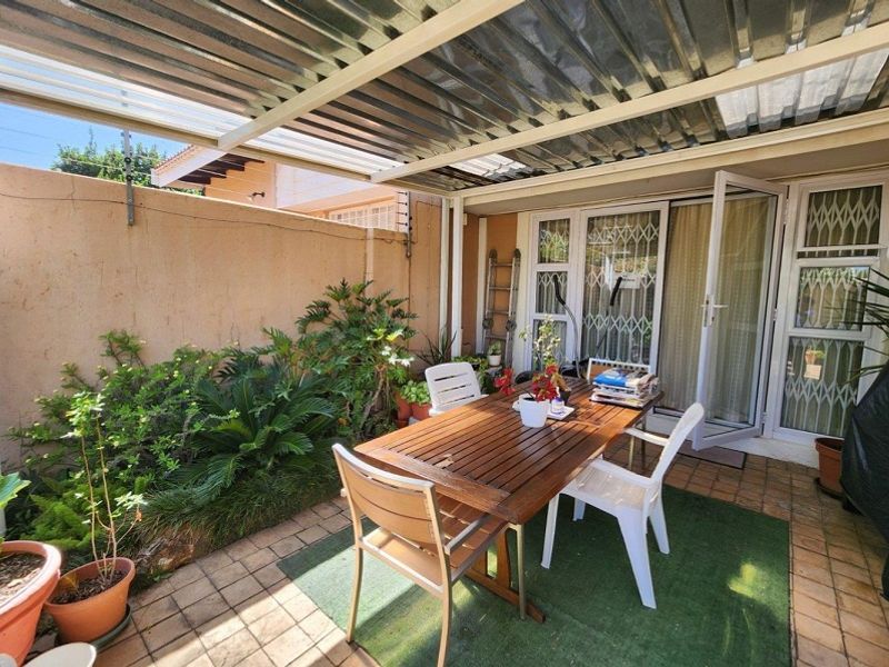 A covered outdoor patio area featuring tiled flooring, a corrugated metal roof, and direct access to the interior through security-fitted glass doors.