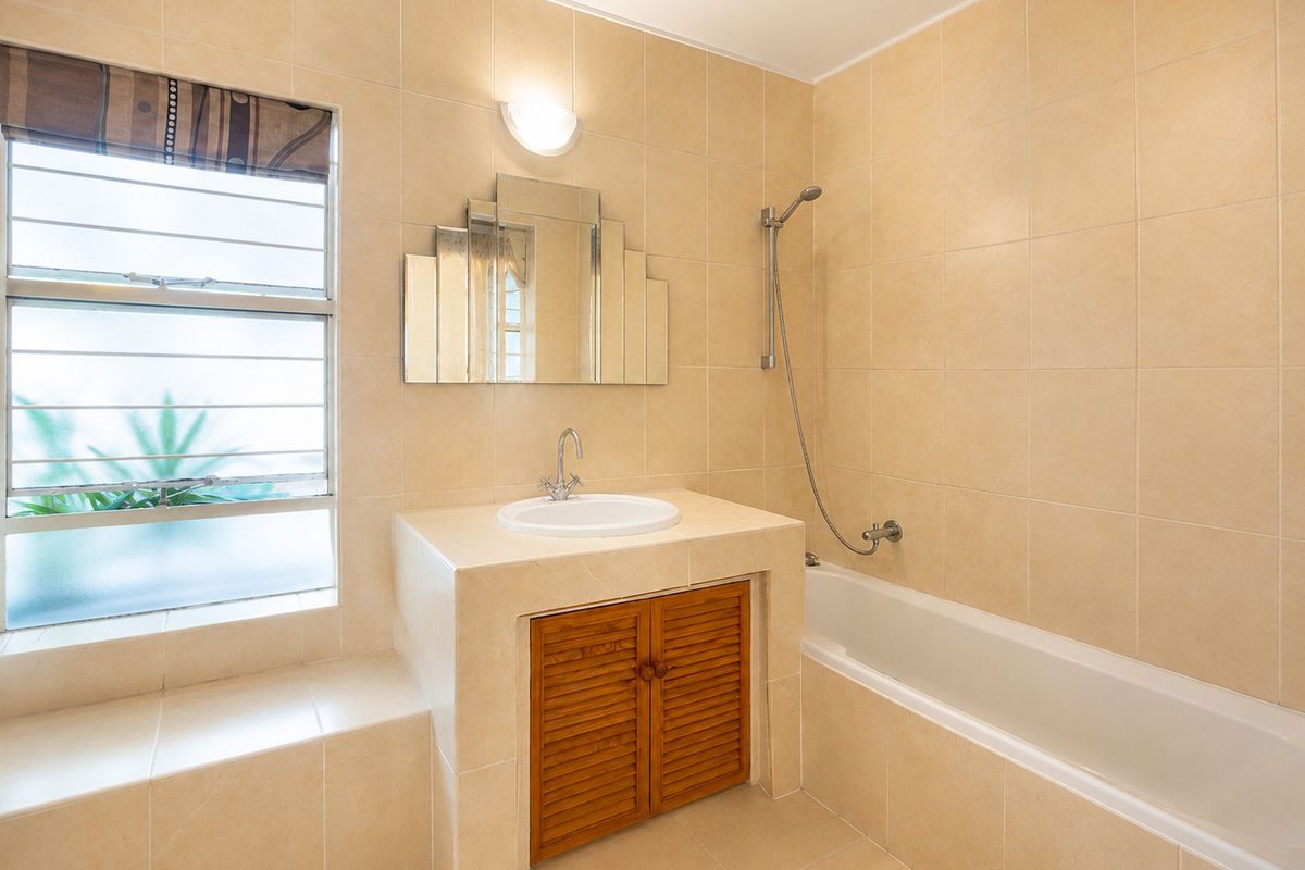 A clean, neutral-toned bathroom featuring a built-in vanity with a drop-in basin, a bathtub with a handheld shower, and full-height wall tiling.