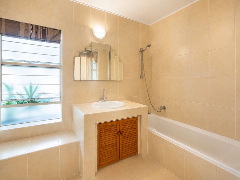 A clean, neutral-toned bathroom featuring a built-in vanity with a drop-in basin, a bathtub with a handheld shower, and full-height wall tiling.