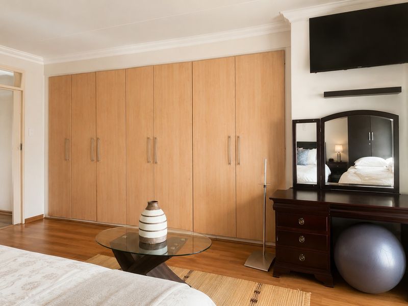 A well-maintained bedroom featuring extensive light wood built-in cupboards, laminate flooring, and decorative coving.