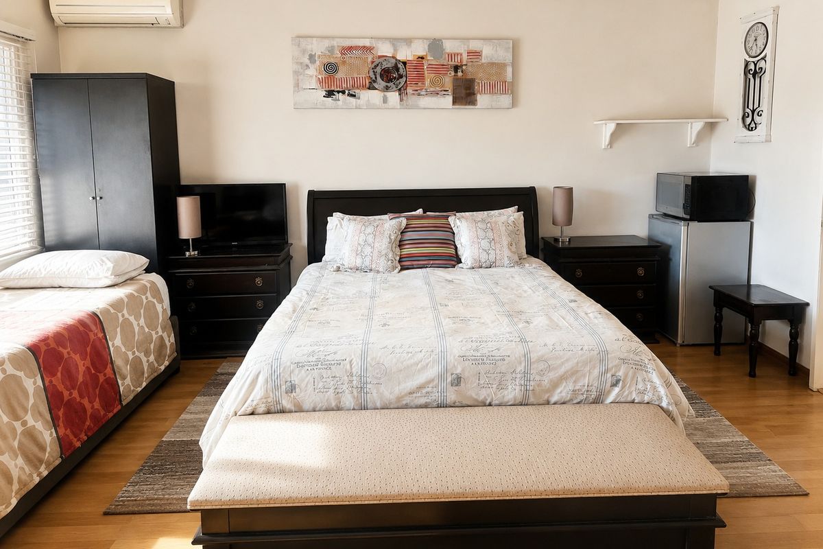 A spacious bedroom featuring laminate flooring, a wall-mounted split-system air conditioner, and venetian blinds.