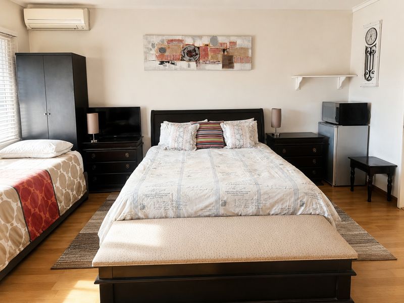 A spacious bedroom featuring laminate flooring, a wall-mounted split-system air conditioner, and venetian blinds.