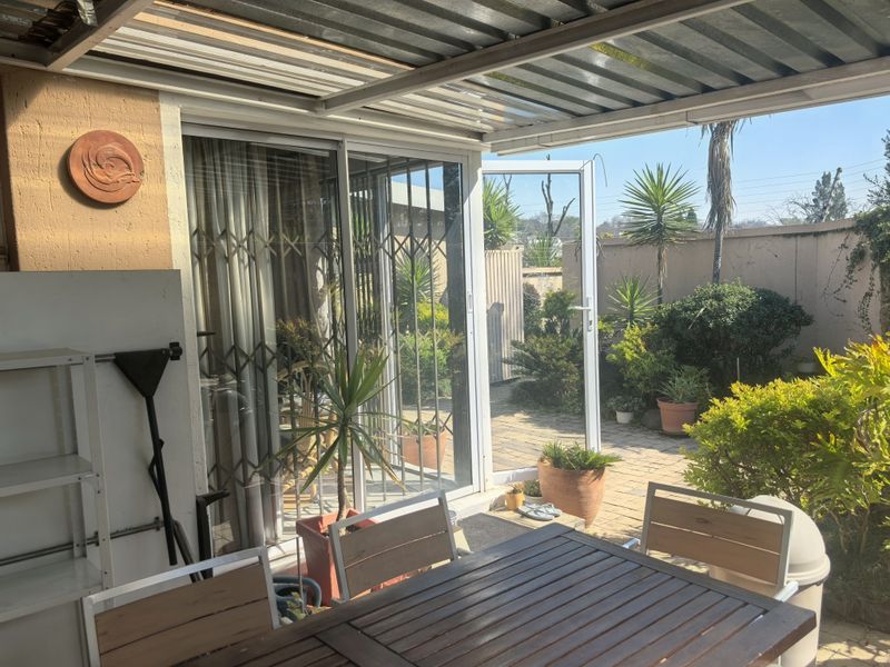 A covered outdoor patio area featuring a corrugated metal roof, sliding glass doors with security gates, and direct access to a paved garden space.