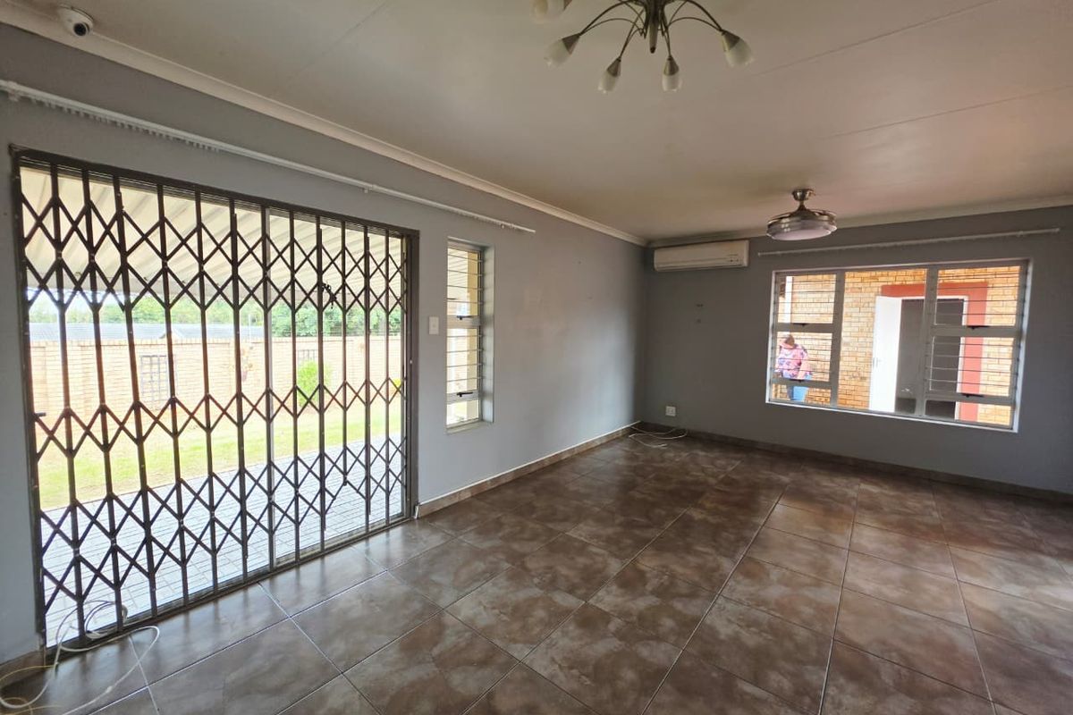 Spacious living area featuring tiled flooring, air conditioning, ceiling fan, and secure access to the exterior via a sliding security gate.