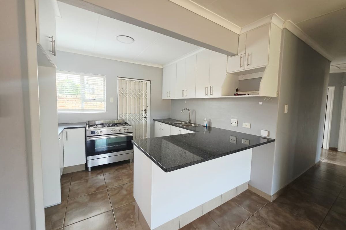 A clean, functional kitchen featuring white cabinetry, dark granite countertops, a stainless steel gas stove, and tiled flooring with a breakfast bar layout.