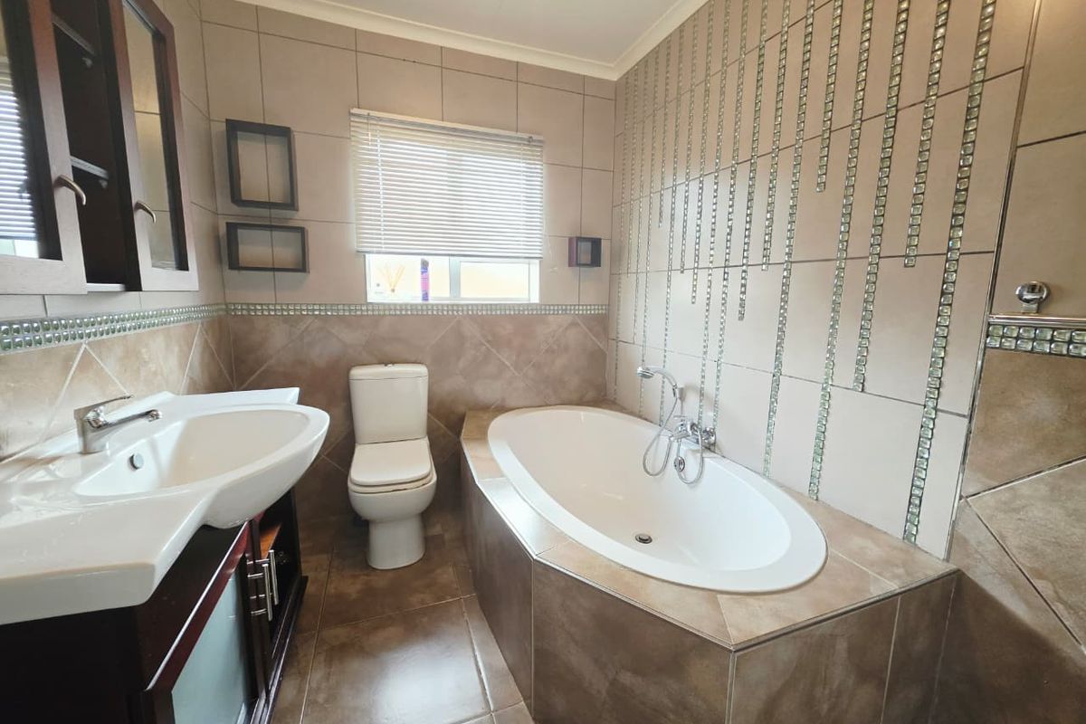 A well-maintained bathroom featuring a built-in bathtub, vanity cabinet with basin, and tiled finishes throughout.