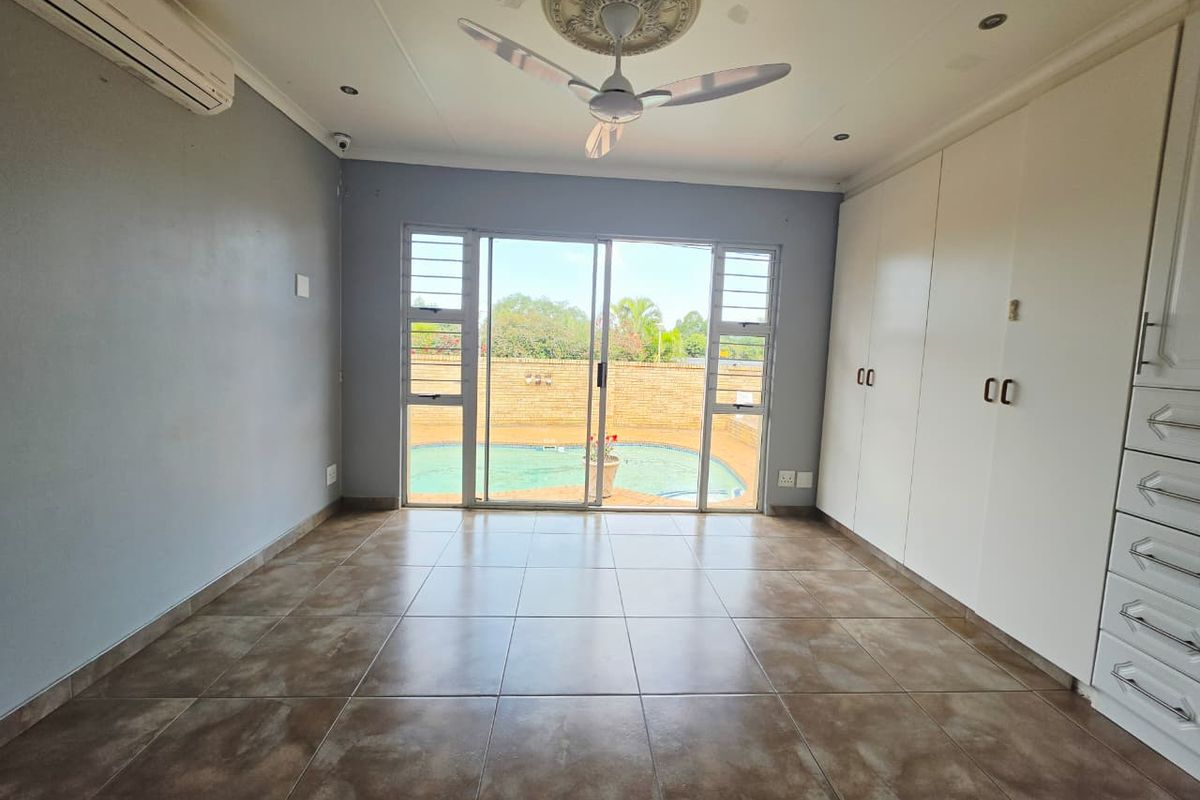 Spacious bedroom featuring built-in cupboards, tiled flooring, and a ceiling fan, with direct access through sliding doors to the outdoor pool area.