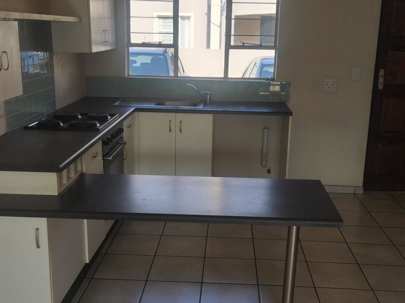 A functional kitchen featuring built-in cabinetry, a breakfast bar, integrated oven and hob, and tiled flooring, offering a practical layout for daily use.