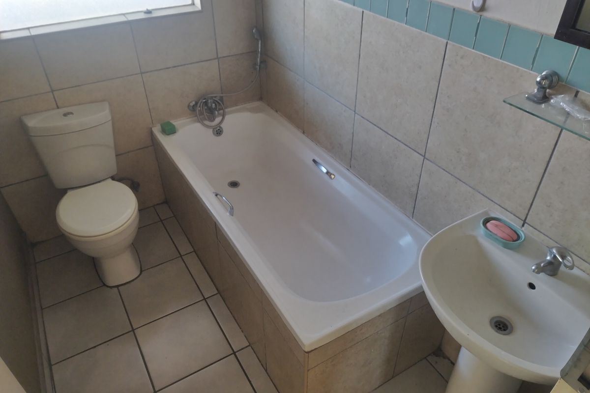 A functional bathroom featuring a standard bathtub, pedestal basin, and toilet with neutral wall and floor tiling.