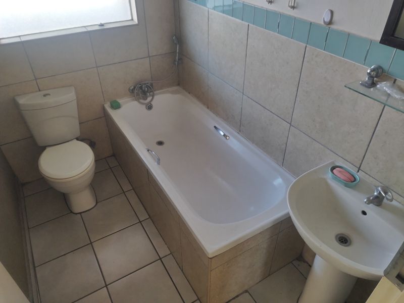 A functional bathroom featuring a standard bathtub, pedestal basin, and toilet with neutral wall and floor tiling.