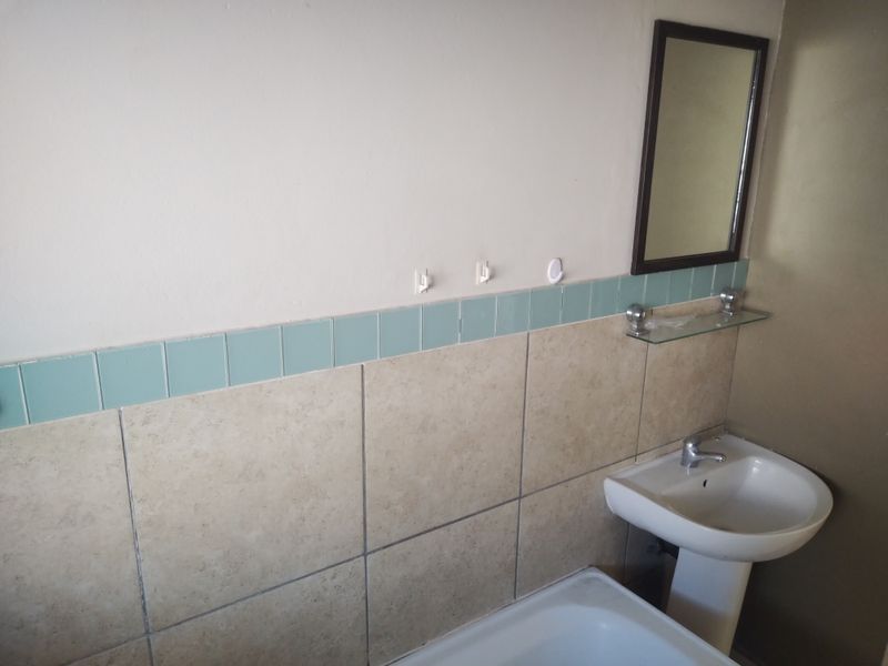 A functional bathroom featuring a pedestal basin, bathtub, and tiled splashback with a wall-mounted mirror and glass shelf.