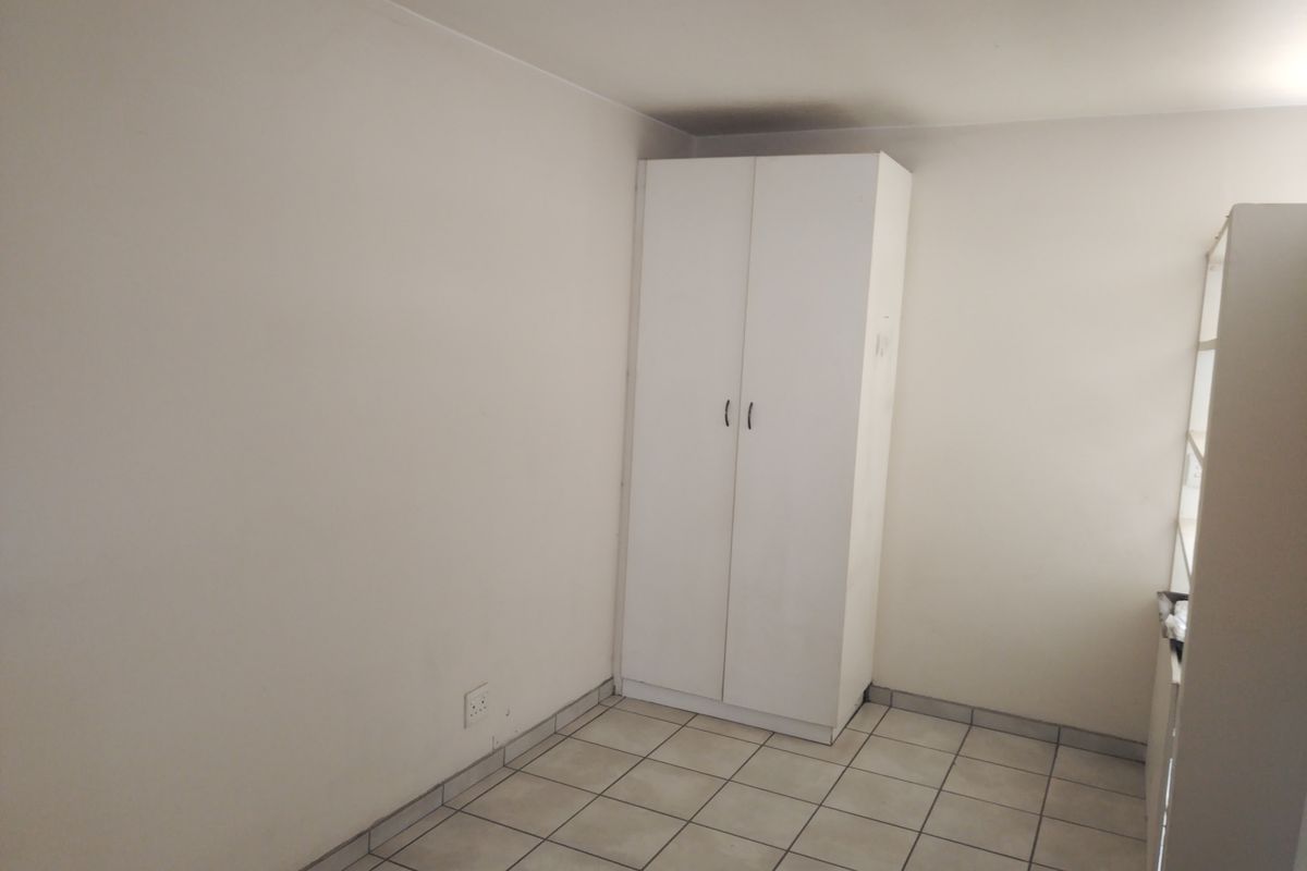 A simple, empty bedroom featuring neutral walls, tiled flooring, and a built-in white wardrobe.