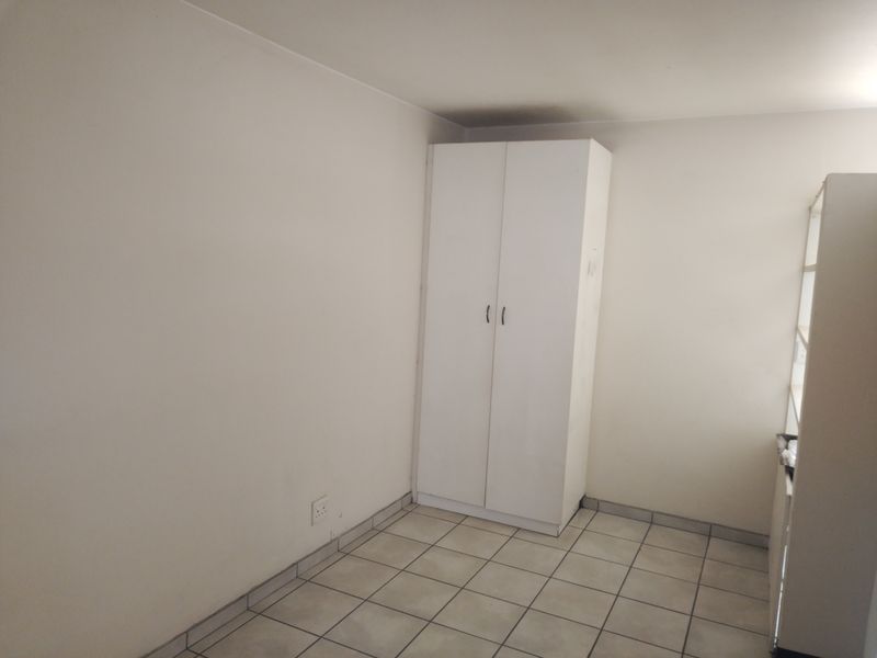 A simple, empty bedroom featuring neutral walls, tiled flooring, and a built-in white wardrobe.