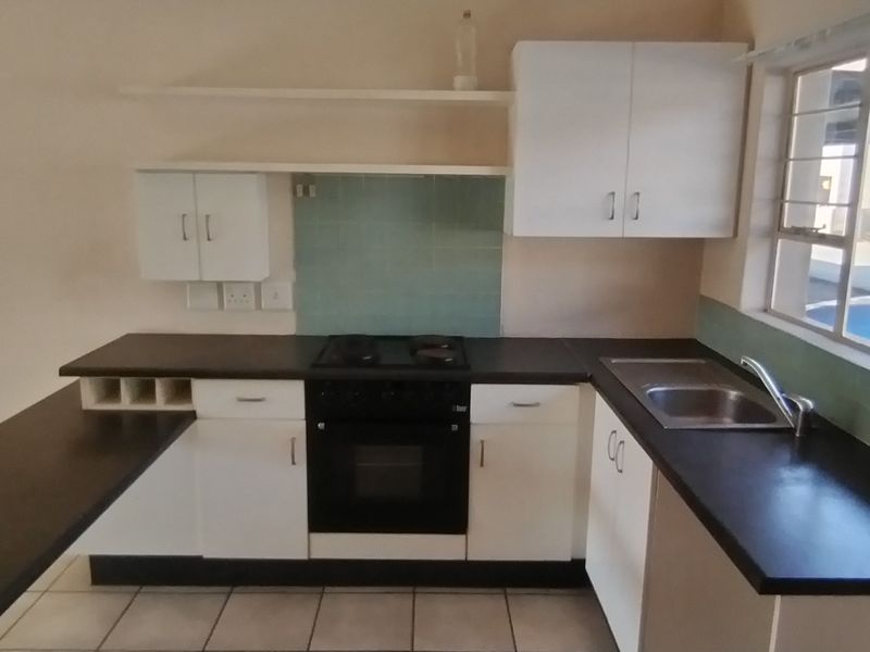 A functional kitchen featuring white cabinetry, dark laminate countertops, a built-in oven with gas hob, and a stainless steel sink.