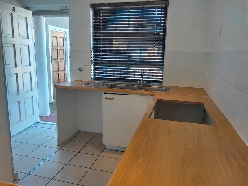 A functional kitchen area featuring laminate countertops, a stainless steel sink, and tiled splashbacks, currently vacant and awaiting new appliances and modern updates.