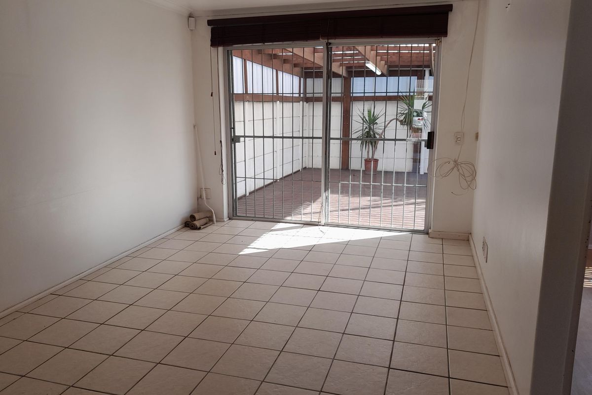 An empty living room featuring tiled flooring and a sliding glass door with security gate, providing direct access to a covered patio area.