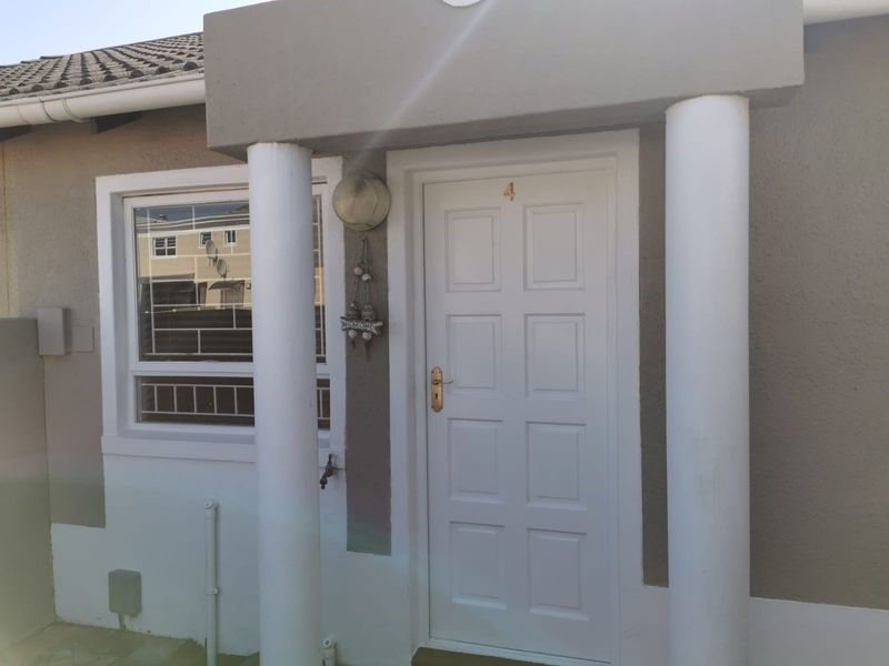 Front entrance of the townhouse featuring a white panelled door, decorative concrete columns, and security bars on the window.