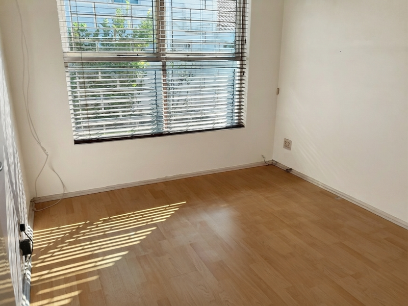 A vacant bedroom featuring light-toned laminate flooring, neutral walls, and venetian blinds, offering a blank canvas for personalization.