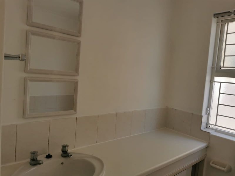 A functional bathroom featuring a vanity basin with tiled splashback and security bars on the window.