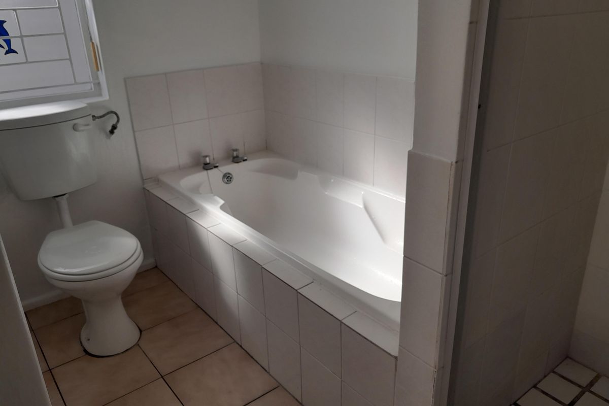 A functional bathroom featuring a built-in bathtub, standard toilet, and neutral ceramic tiling throughout.