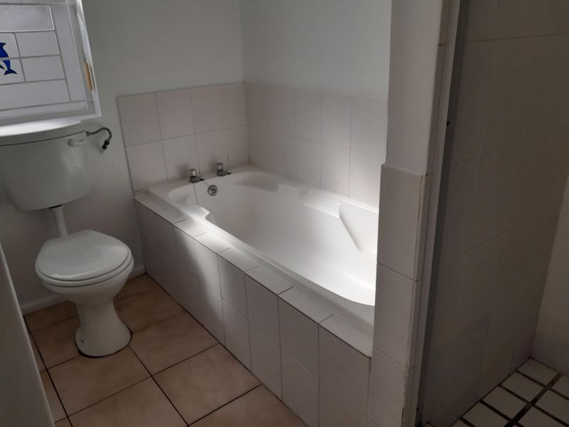 A functional bathroom featuring a built-in bathtub, standard toilet, and neutral ceramic tiling throughout.