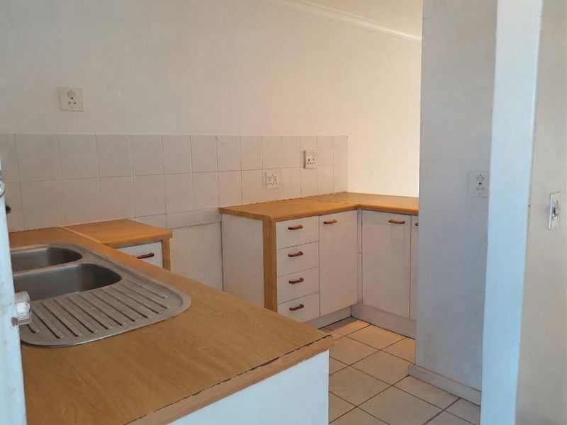 A compact, empty kitchen featuring laminate countertops, a double bowl stainless steel sink, tiled backsplash, and white cabinetry with wood trim.