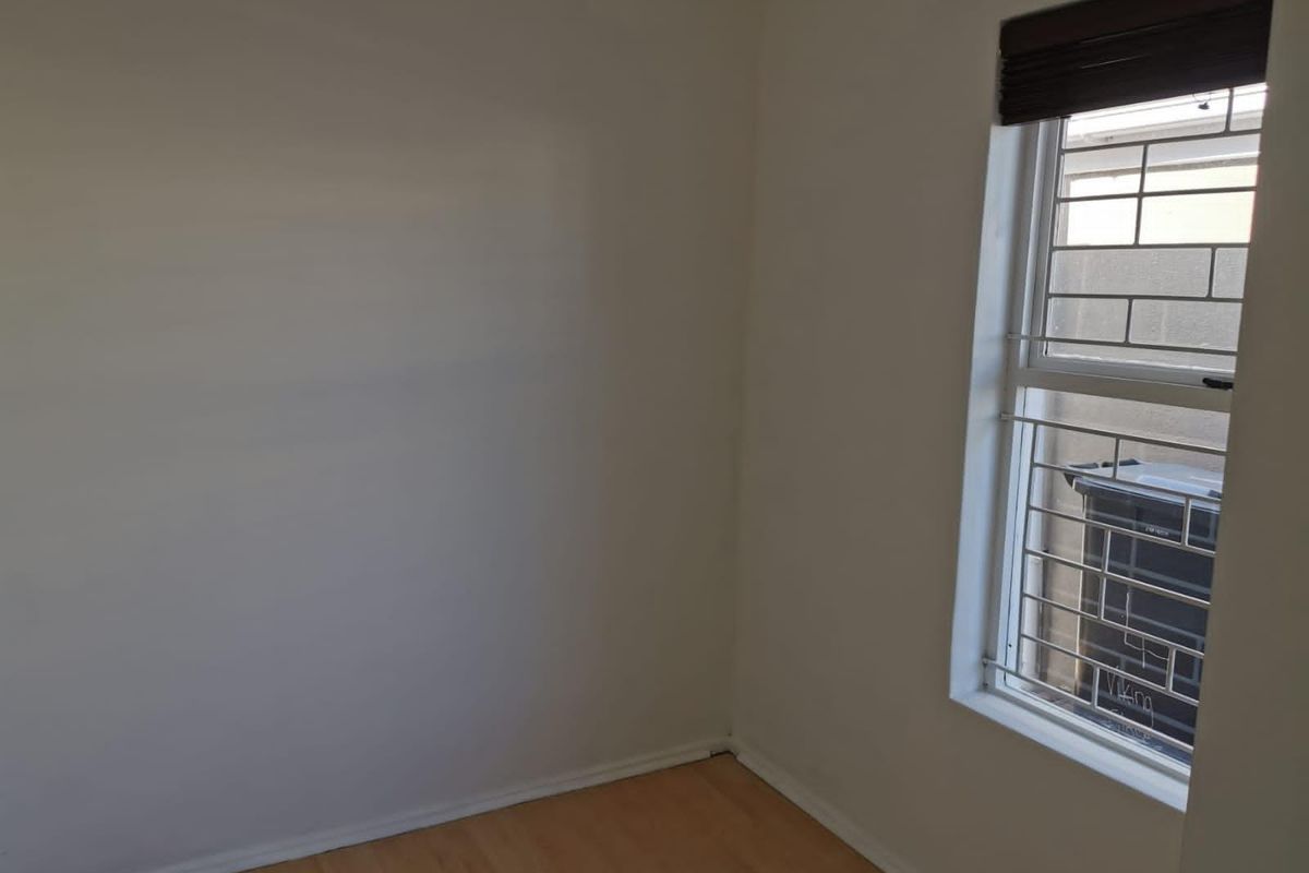 A clean, empty bedroom featuring light laminate flooring and a window fitted with security bars and a blind.