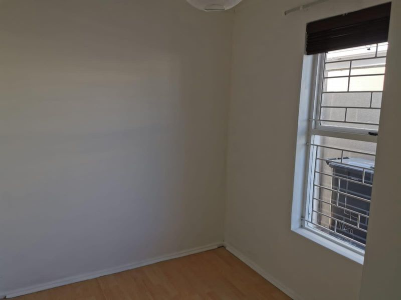 A clean, empty bedroom featuring light laminate flooring and a window fitted with security bars and a blind.