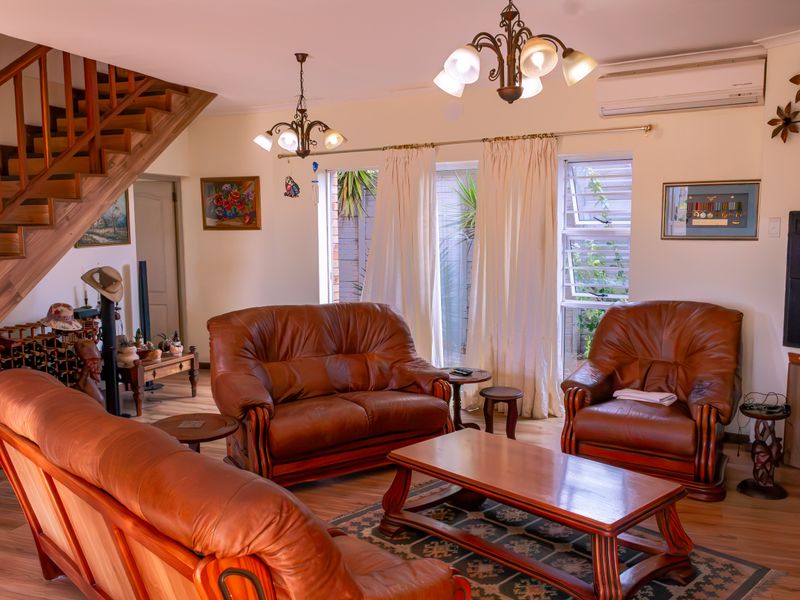 A comfortable living room featuring wooden flooring, a staircase, and a split-system air conditioner, offering a warm and functional space.