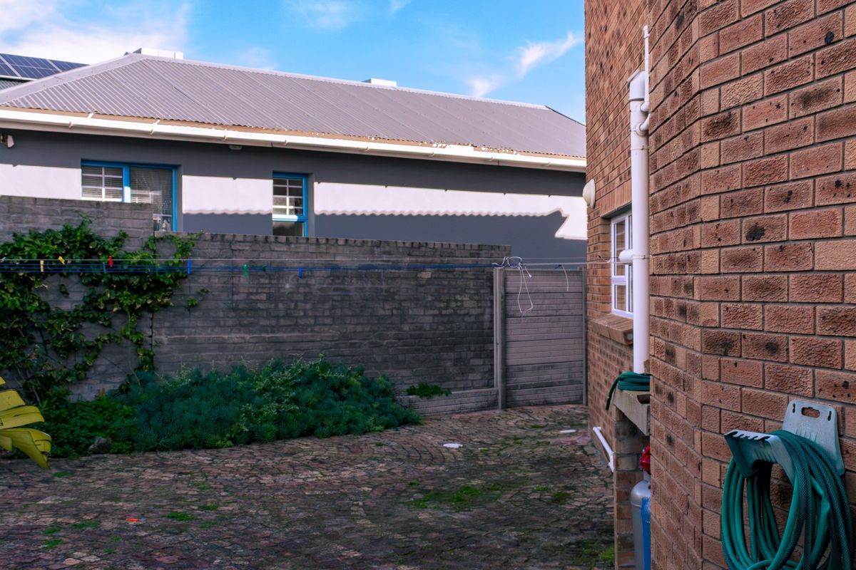 A rear exterior view showing a brick-walled house facade, cobblestone paved courtyard, and boundary wall with established garden greenery.