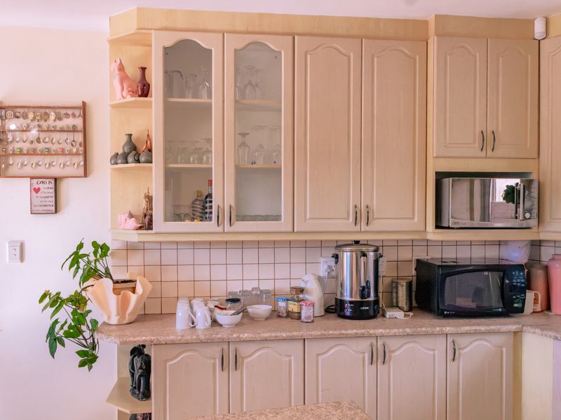 A functional kitchen area featuring light-toned built-in cabinetry, laminate countertops, and a classic ceramic tile backsplash with integrated microwave housing.