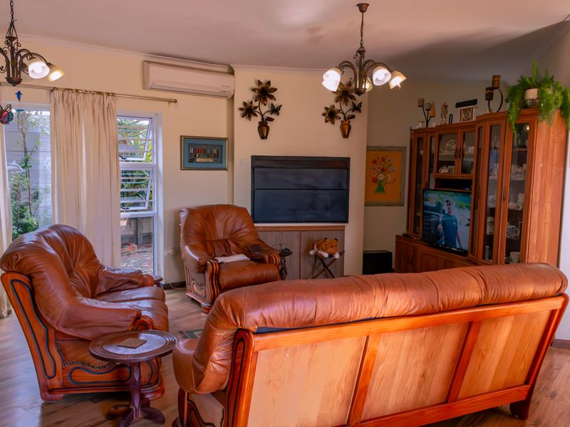 A comfortable living room featuring laminate flooring, a wall-mounted air conditioning unit, and natural light through side windows.
