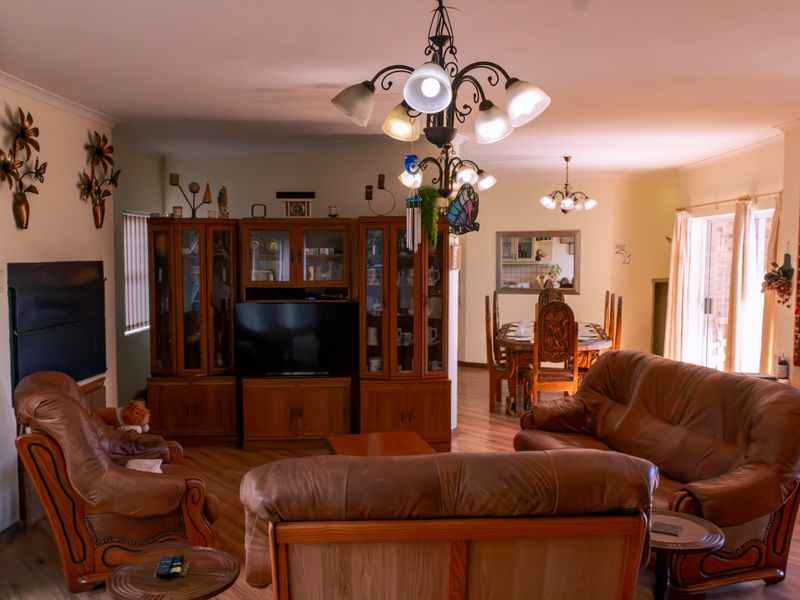 Spacious open-plan living and dining area featuring laminate flooring, a decorative chandelier, and sliding glass doors leading to the exterior.