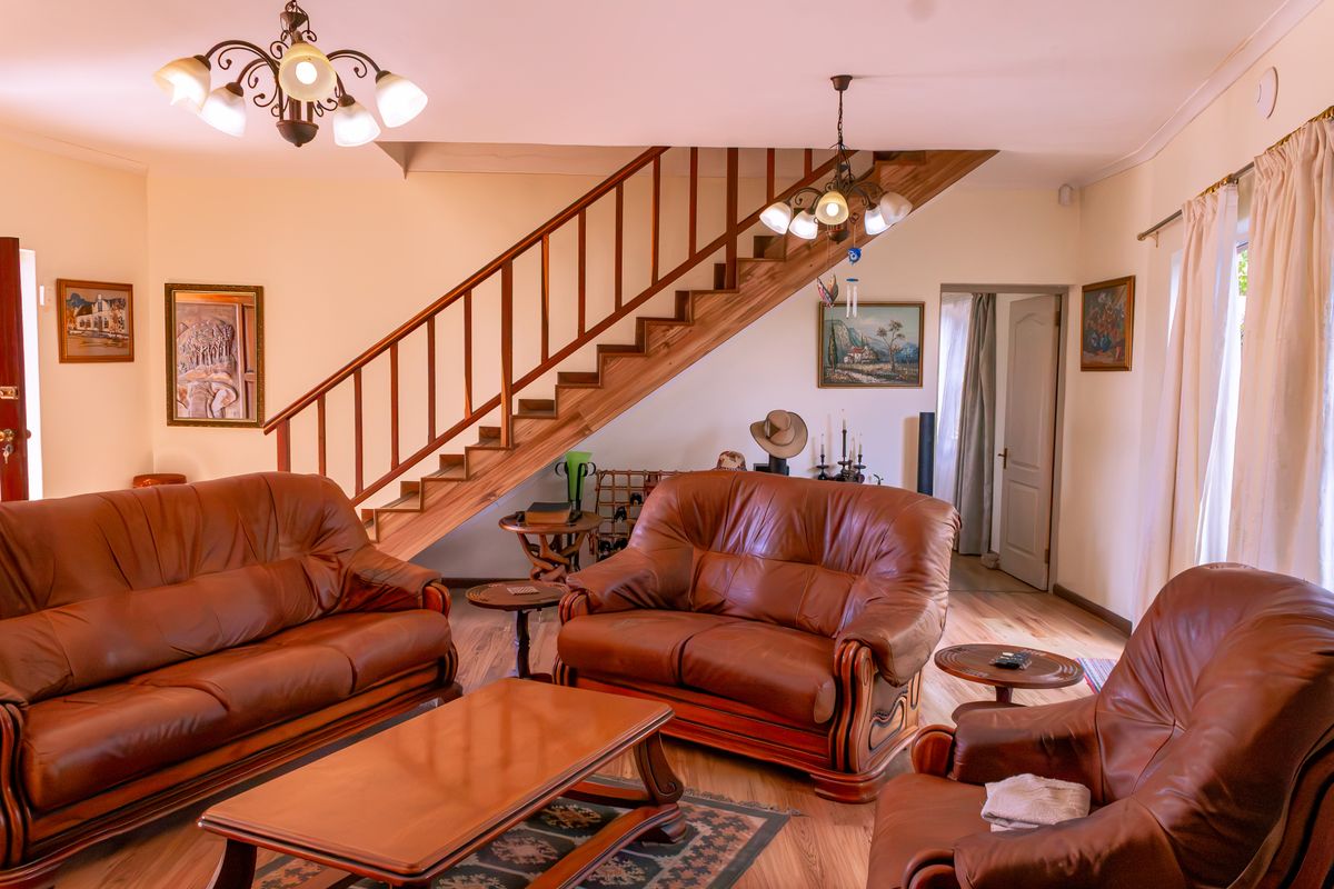 A spacious living room featuring a prominent wooden staircase with a balustrade, laminate flooring, and traditional ceiling light fixtures.