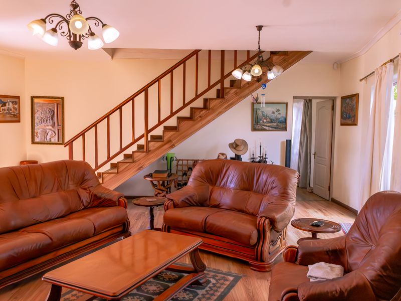 A spacious living room featuring a prominent wooden staircase with a balustrade, laminate flooring, and traditional ceiling light fixtures.