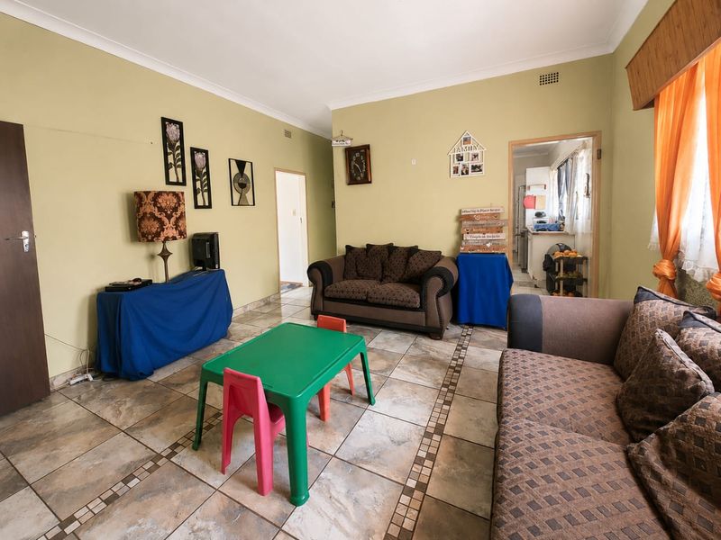 A living room featuring tiled flooring and neutral wall paint, providing a functional space with direct access to the kitchen area.