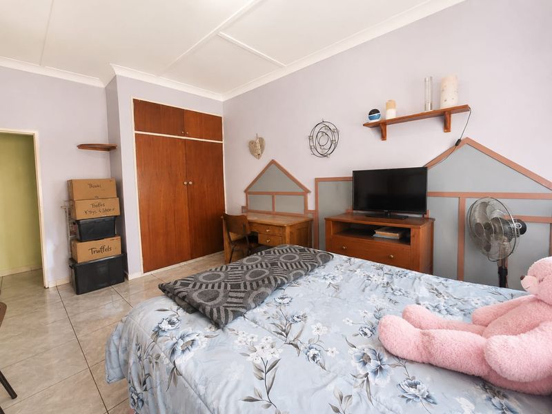 A bedroom featuring tiled flooring, built-in wooden wardrobes, and decorative wall paneling, offering a functional space with potential for modern updates.