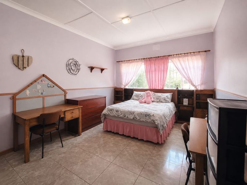A spacious bedroom featuring tiled flooring, built-in headboard shelving, and a large window with natural light.