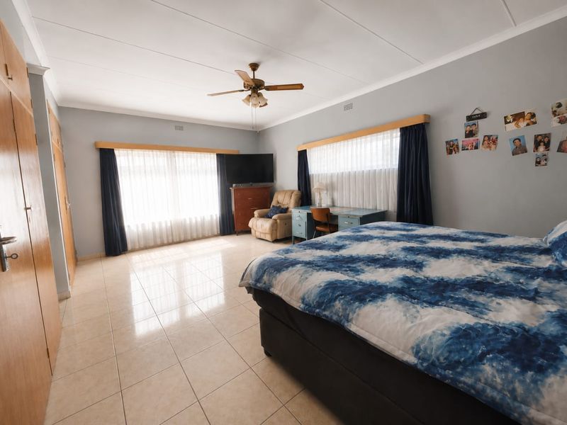 Spacious bedroom featuring tiled flooring, built-in cupboards, and a ceiling fan, offering a functional layout with ample natural light.