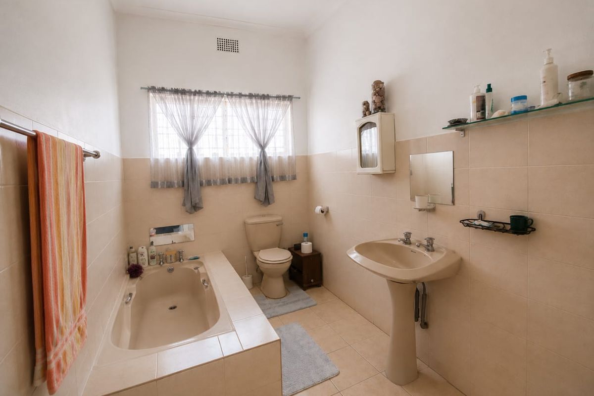 A functional bathroom featuring a built-in bathtub, pedestal basin, and toilet with neutral ceramic tiling throughout.