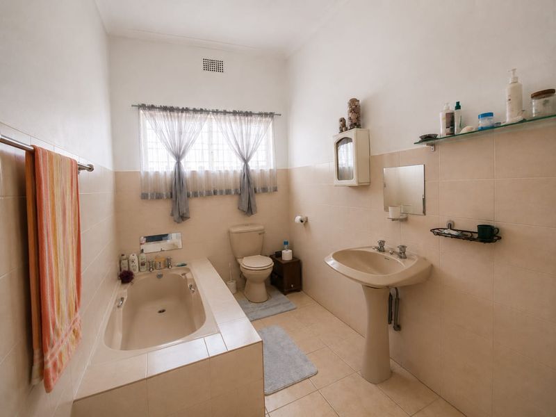 A functional bathroom featuring a built-in bathtub, pedestal basin, and toilet with neutral ceramic tiling throughout.