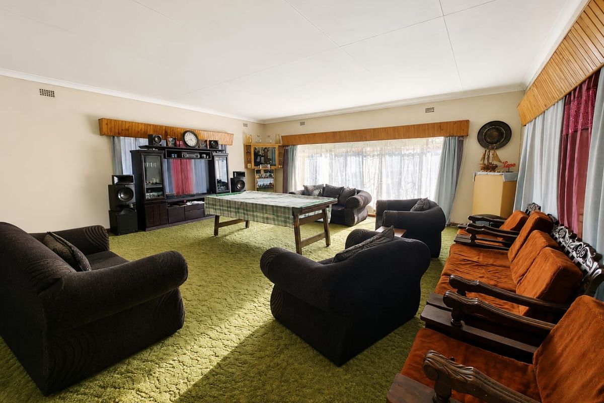 Spacious living room featuring large windows, timber pelmets, and carpet flooring, offering a versatile area for relaxation and entertainment.