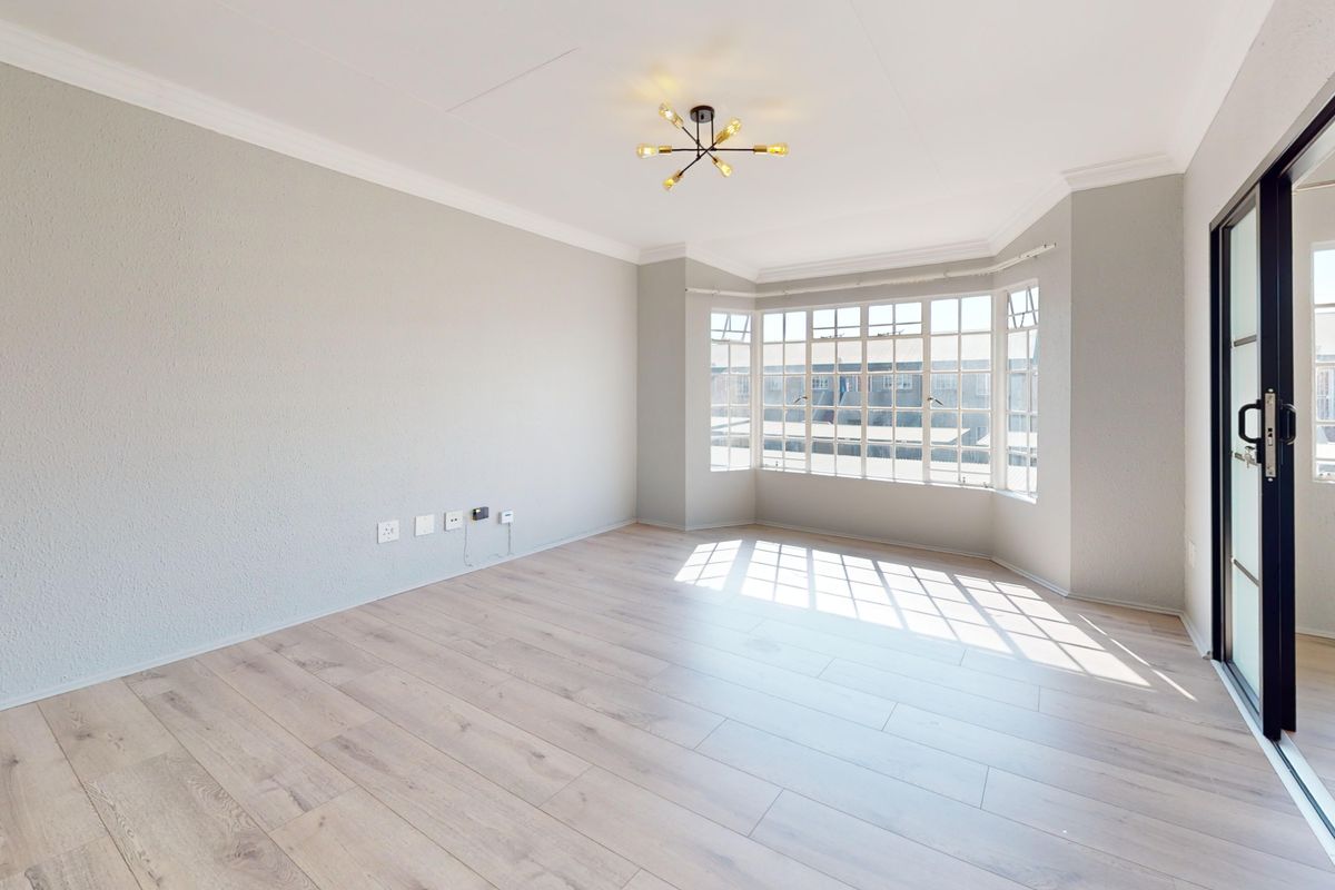 A bright and spacious empty living room featuring modern laminate flooring, a large bay window, and a sliding glass door leading to the exterior.