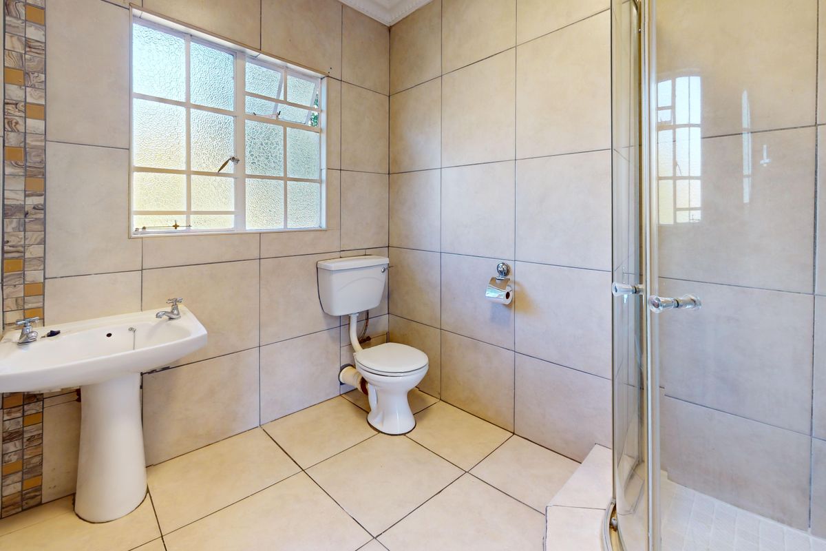 A functional bathroom featuring a pedestal basin, toilet, and a glass-enclosed shower with neutral floor-to-ceiling wall tiles.