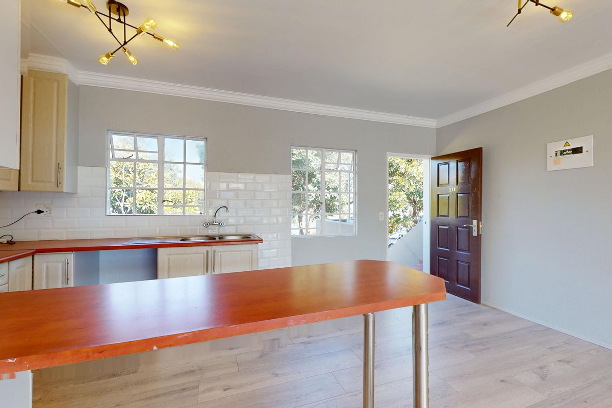 Open-plan kitchen and living area featuring laminate flooring, subway tile backsplash, and a breakfast bar, with direct access to the entrance.