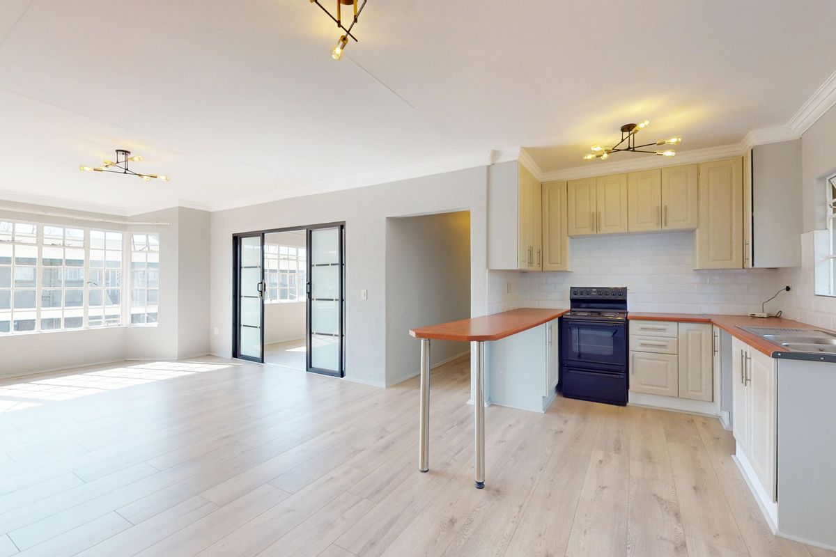 Spacious open-plan living area featuring light laminate flooring, a functional kitchen with breakfast bar, and sliding doors leading to an adjacent space.
