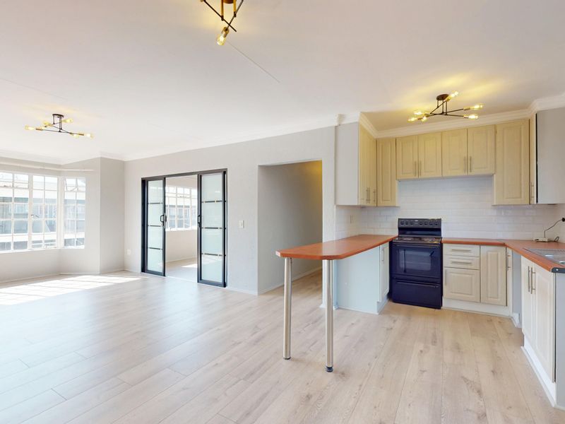 Spacious open-plan living area featuring light laminate flooring, a functional kitchen with breakfast bar, and sliding doors leading to an adjacent space.