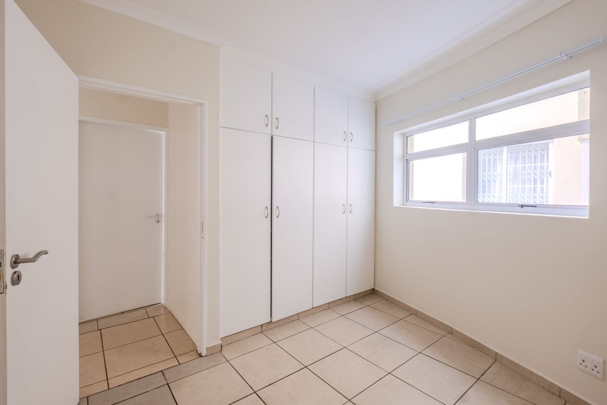 A bright, empty bedroom featuring neutral tiled flooring and ample built-in cupboard storage space.
