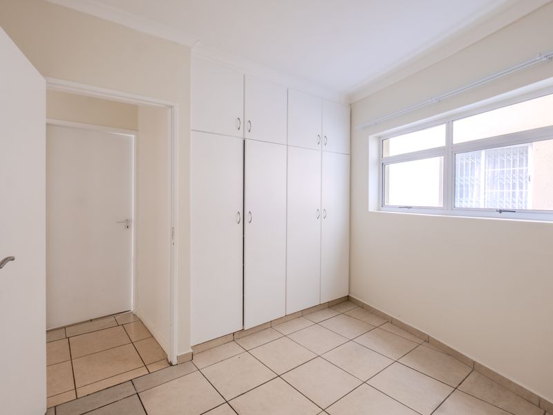 A bright, empty bedroom featuring neutral tiled flooring and ample built-in cupboard storage space.