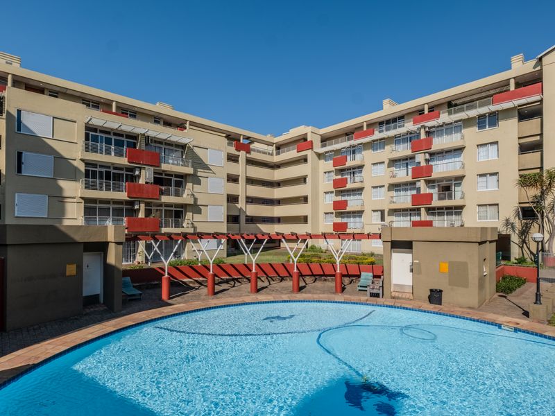 A well-maintained communal swimming pool area featuring a pergola and surrounding apartment building facades with balconies.
